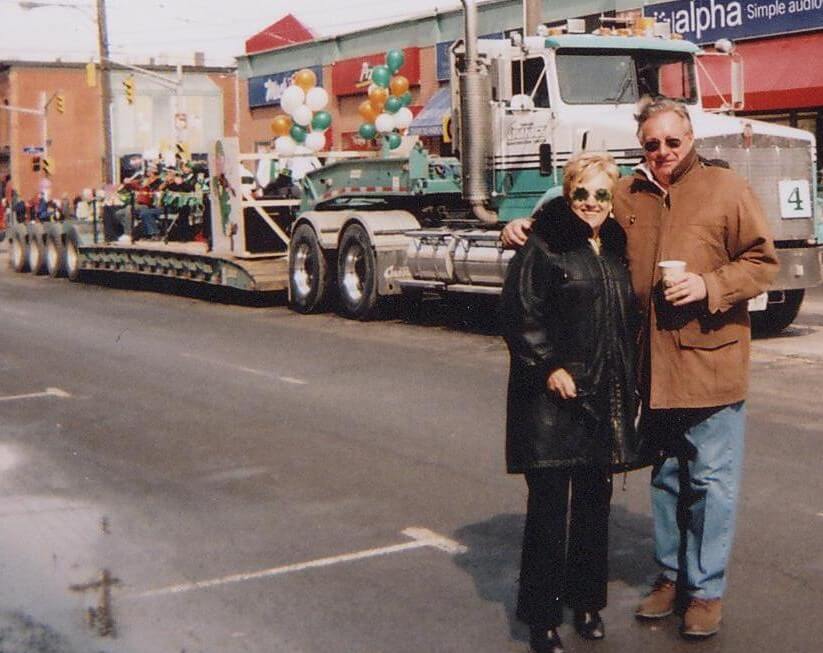 Founders Tom and Kay Cavanagh standing in front of a heavy transport trailer during a community event in Eastern Ontario.
